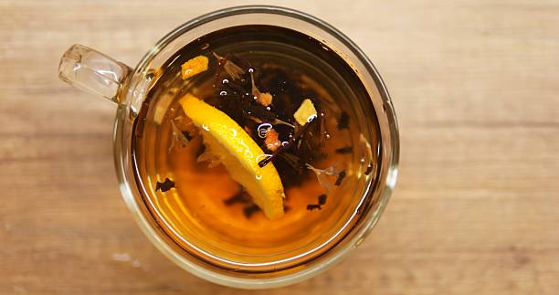 Person throws fresh lemon slice into transparent mug with aromatic black tea