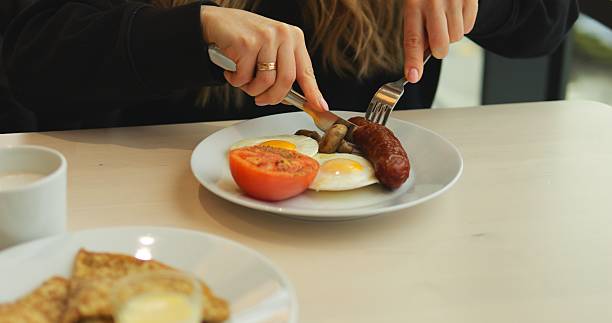 istock Woman cuts sausage and enjoys delicious breakfast while sitting at table 2223937466
