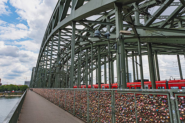 Cologne, Germany - July 20 2023:  Love locks on Hohenzollern Bridge with red trains and steel arches