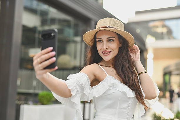 istock Beautiful Female in Elegant Outfit Taking Selfie While Adjusting Her Sun Hat 2223938443