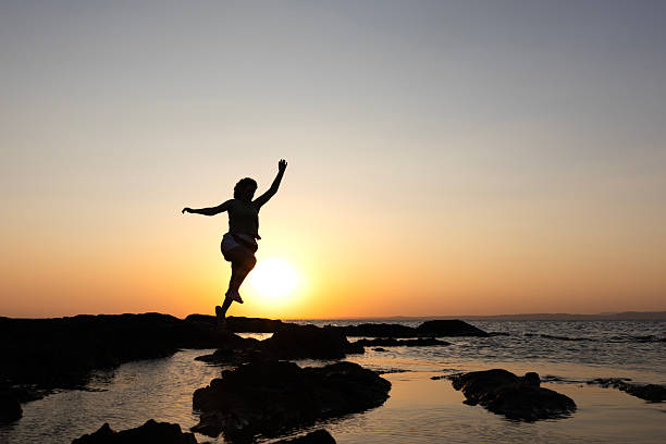 A person captured mid-dance near the ocean during a colorful sunset.