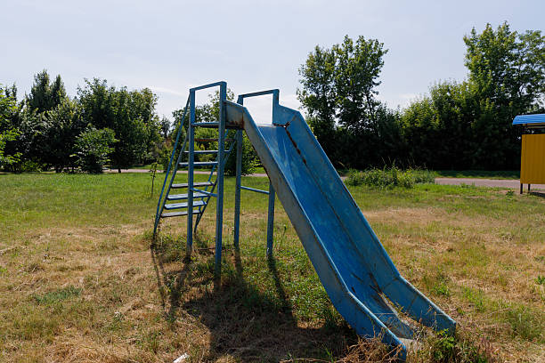 This image captures an empty blue slide, its sturdy metal structure standing in a lush green park, with trees providing shade around it in a serene outdoor environment.
