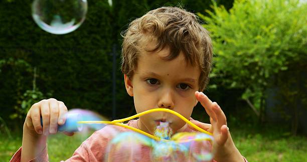 istock Preschooler boy squeezes plastic frame increasing size of bubbles blowing 2223943016