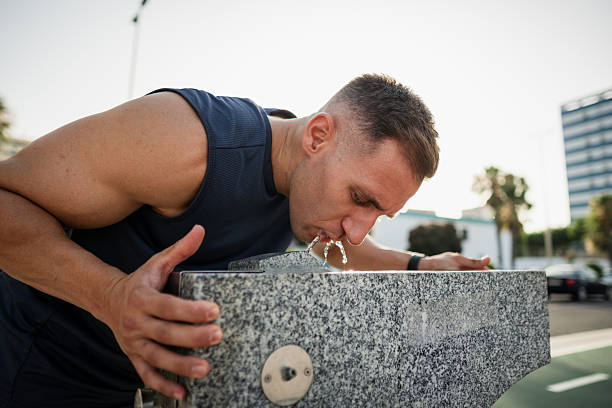 Young sportsman refreshing himself by drinking water from a public fountain after training