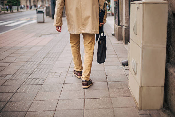 Back view of a senior man lower part of body walking on the street. He wears ocher pants and an ocher jacket.