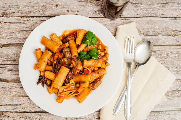 Plate of hearty beef stew served over rigatoni pasta with vegetables and a garnish of parsley