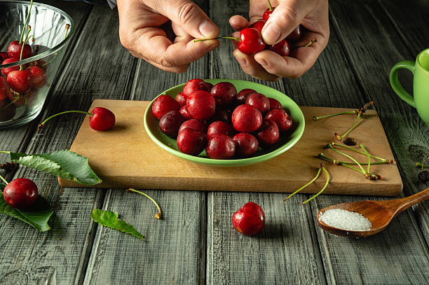 istock Hands meticulously remove stems from ripe cherries in a cozy kitchen. A vibrant bowl of cherries is surrounded by kitchen items, creating a warm atmosphere for cooking 2223957029