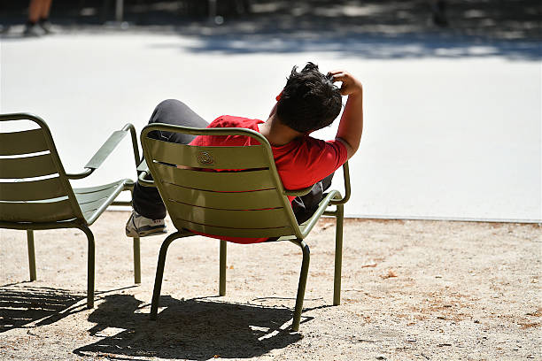 Paris, France - April 9, 2025: A woman sits in the sun on the pavement reading Le Canard Enchaine in the Palais Royal.