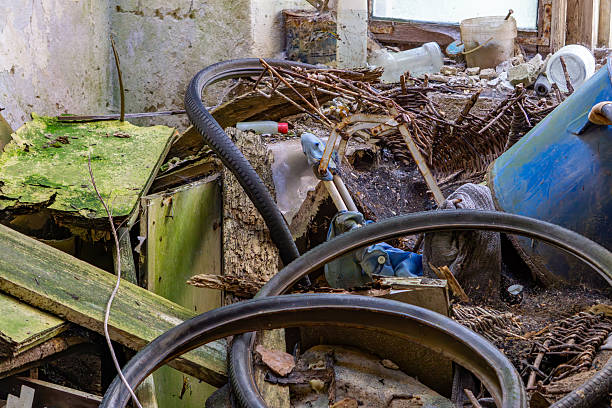 Abandoned interior filled with tangled hoses, rusty tools, broken furniture, and scattered debris, showing signs of decay and neglect