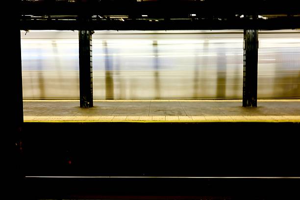A silver subway train streaks past the platform, its rapid movement captured as a horizontal blur between iron columns.
