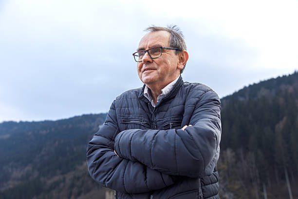 Mature caucasian male in jacket standing by stone wall in mountain landscape