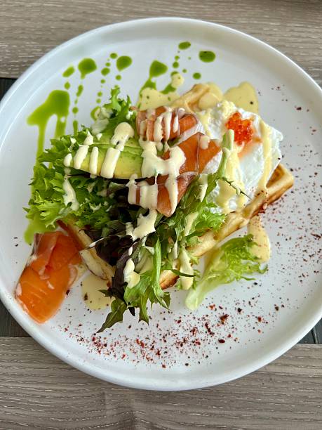 Wafle topped with smoked salmon, avocado slices, poached egg and mixed greens