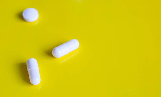 istock Several white pills of different shapes – one round and two capsules – are arranged on a bright yellow background. 2223980165