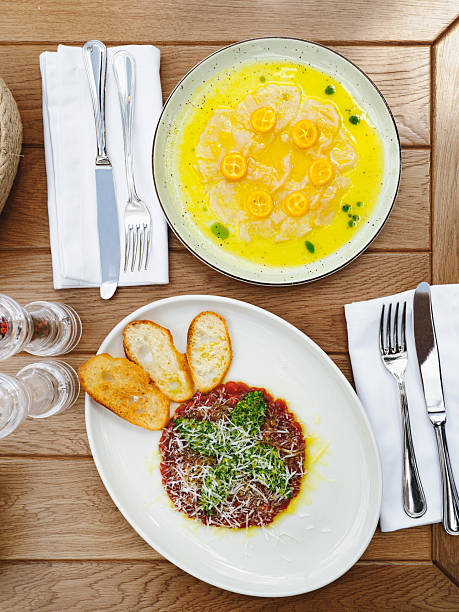 Fresh sea bream carpaccio with salad and tuna or beef tartar with pesto sauce and parmesan cheese. Two types of antipasti appetizers on wooden table, top view or flat lay