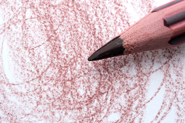 A close-up view of a red pencil creating swirls on textured white paper.