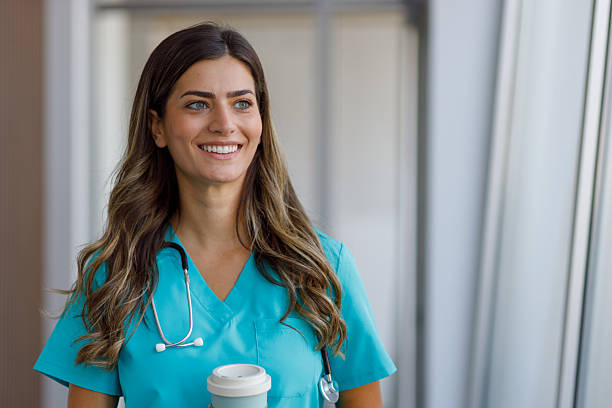 istock Friendly female nurse in blue scrubs drinking takeaway coffee, turning head sideways 2223988183