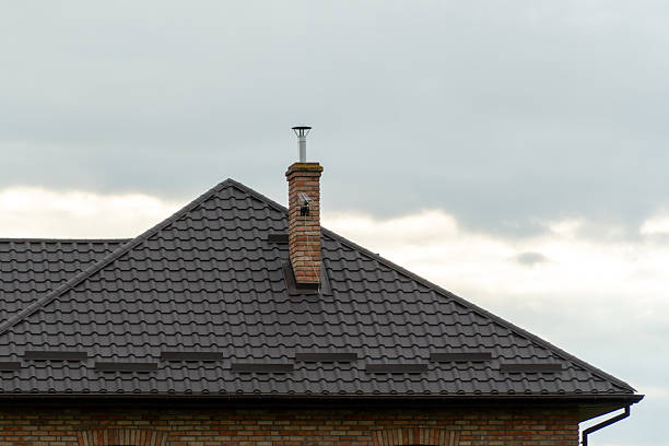 istock A distinctive brick chimney rises from a patterned tiled roof amidst a backdrop of gray clouds, showcasing suburban architecture and weather 2224000380