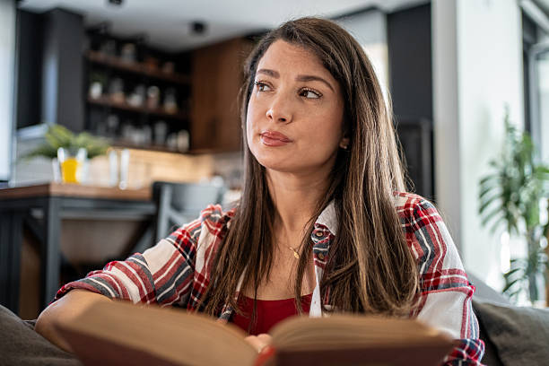 istock Young woman reading a book and thinking at home 2224006317