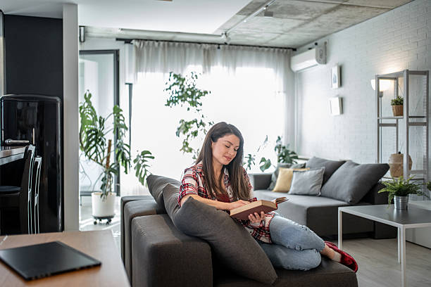 istock Young woman relaxing on sofa reading a book in modern apartment 2224006326