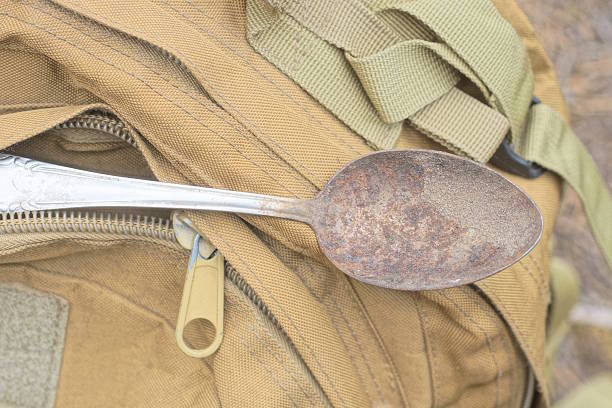 one old gray rusty metal spoon lies on in pocket brown fabric backpack in the street