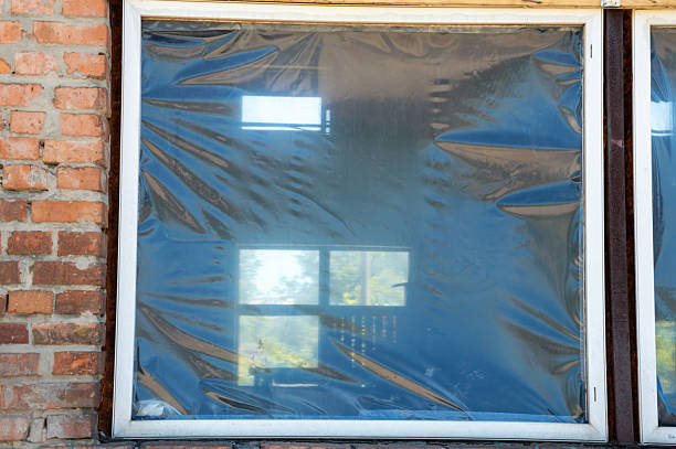 istock A window covered with plastic wrap shows reflections of sunlight and greenery, indicating neglect in an abandoned structure 2224007176