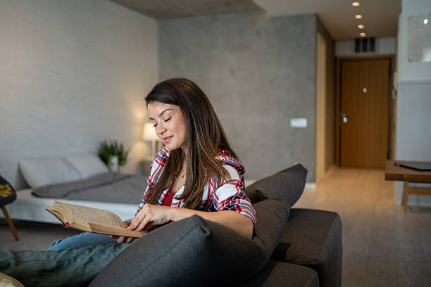 istock Young woman reading a book on the sofa at home 2224007627
