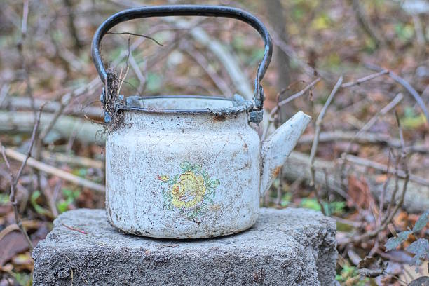 one old dirty white enamel metal teapot stands on a gray table on a summer street