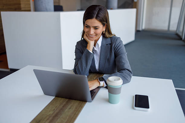 istock Smiling businesswoman using laptop, enjoying coffee break at workplace, modern office interior, technology and productivity concept 2224008423