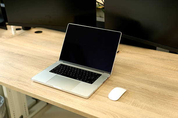 Laptop and mouse sitting on a desk, ready for work, with two monitors in the background