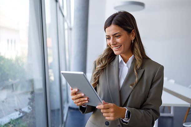 istock Smiling businesswoman engaging with a digital tablet, enjoying online work while surrounded by a modern office environment 2224010710