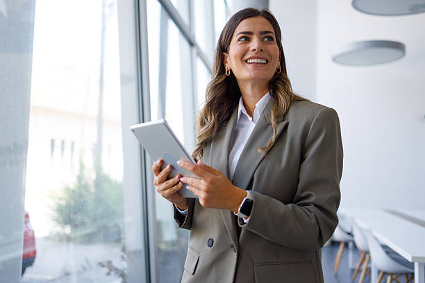 istock Professional businesswoman working on digital tablet, smiling confidently while standing in minimalist corporate workspace 2224010768