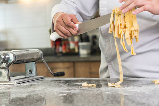 Chef preparing fresh pasta in a professional kitchen, cutting dough with a knife