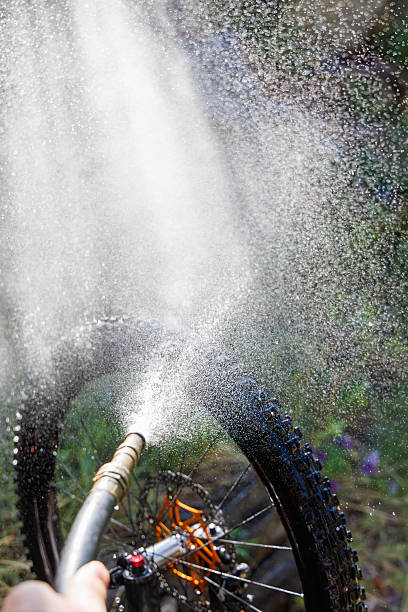A close-up view of washing a mountain bike tire with water from a garden hose.