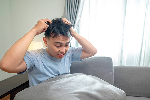 istock Indonesian southeast asian man sitting on the couch and scratching his head. Problem of dandruff. Healthcare concept 2224027996