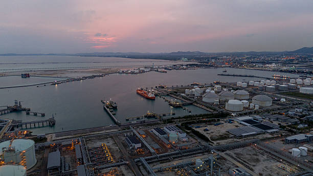 istock large oil tanker docked at a refinery terminal with multiple white storage tanks, complex pipeline networks, and offshore loading platforms. Represents global oil logistics 2224034337