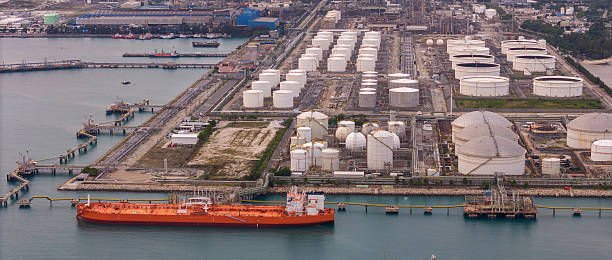 istock large oil tanker docked at a refinery terminal with multiple white storage tanks, complex pipeline networks, and offshore loading platforms. Represents global oil logistics 2224034368