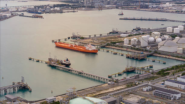 istock large oil tanker docked at a refinery terminal with multiple white storage tanks, complex pipeline networks, and offshore loading platforms. Represents global oil logistics 2224034371