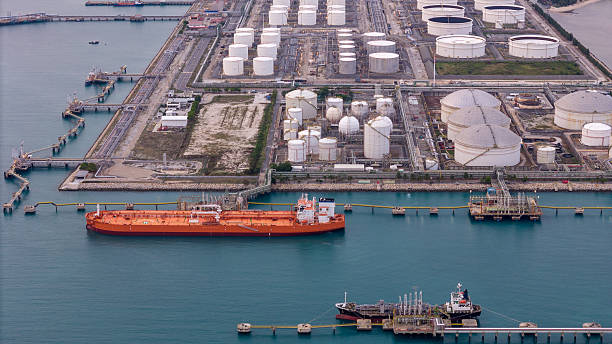 istock large oil tanker docked at a refinery terminal with multiple white storage tanks, complex pipeline networks, and offshore loading platforms. Represents global oil logistics 2224034820