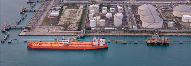 istock large oil tanker docked at a refinery terminal with multiple white storage tanks, complex pipeline networks, and offshore loading platforms. Represents global oil logistics 2224034821
