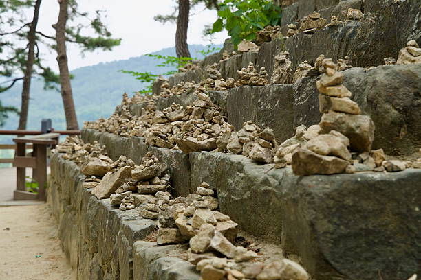 Buyeo County, South Korea - June 13th 2025: Small piles of stones are carefully stacked along the ancient steps of Nakwaam Rock, symbolizing wishes and prayers in a quiet forest setting.