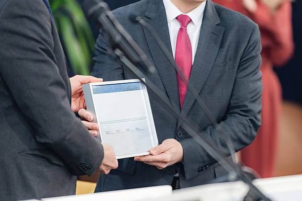 istock Speakers holding a framed certificate at a media conference highlight achievement. Their clear presentation fosters media engagement and public recognition with transparent communication. 2224043428