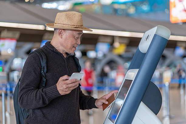 istock asian senior man passenger using smartphone,doing self check in at self service check in machine or KIOSK at the airport terminal 2224043460