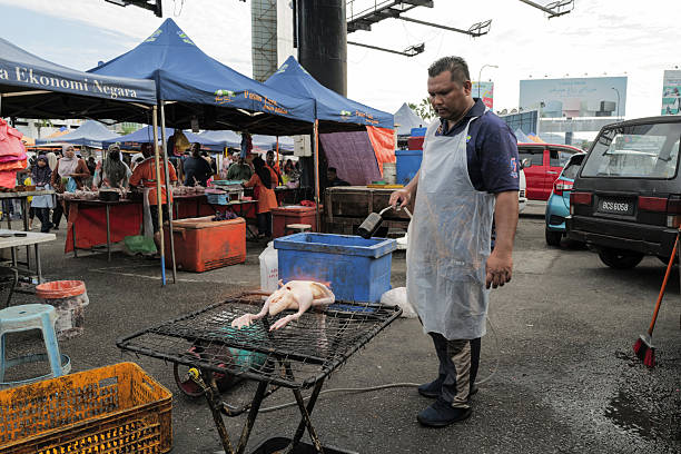 This photo taken on May 25, 2025 shows a man roasting a duck to sell at the Farmers Market also known as Pasar Tani in Kuantan, Pahang. Pasar Tani is open every Sunday from morning until noon. There are various essential goods sold by the vendors here.