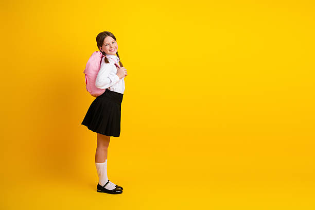Charming Schoolgirl with Pink Backpack in Formal Uniform Smiling on Solid Yellow Background Promoting Education and Back-to-School Themes