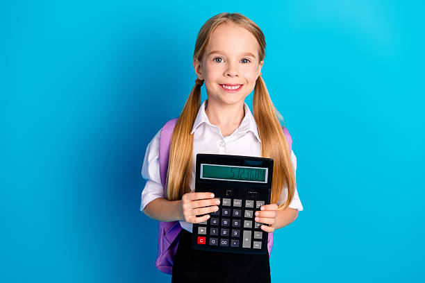 istock Smiling female student holding a large calculator against a bright blue background with ponytails and school uniform 2224050039