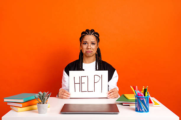 istock Teen holding help sign in vibrant classroom setting expressing frustration with homework against orange wall decor 2224051473