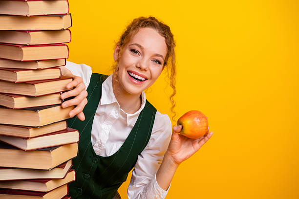 istock Charming female student holding an apple with a stack of books in a cheerful educational setting 2224051659