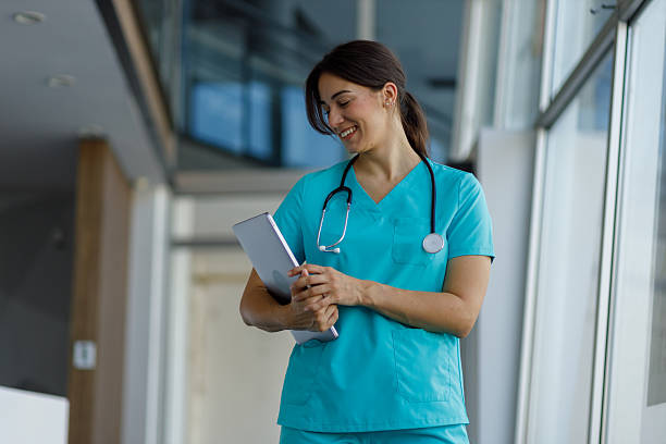 istock Female doctor wearing blue scrubs and stethoscope smiling while using digital tablet in modern hospital corridor 2224053342