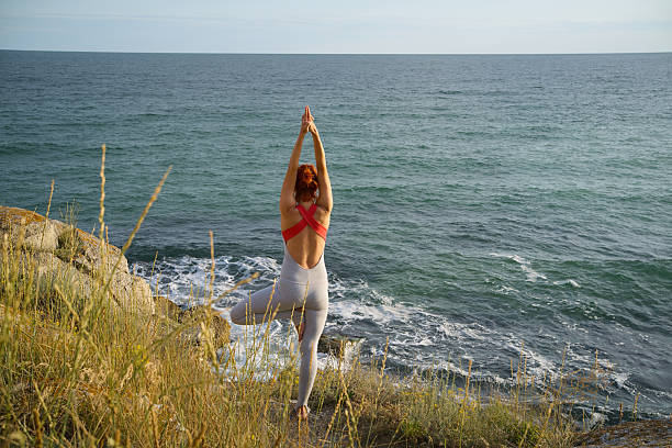 Woman Practicing Yoga Tree Pose by the Sea at Sunset