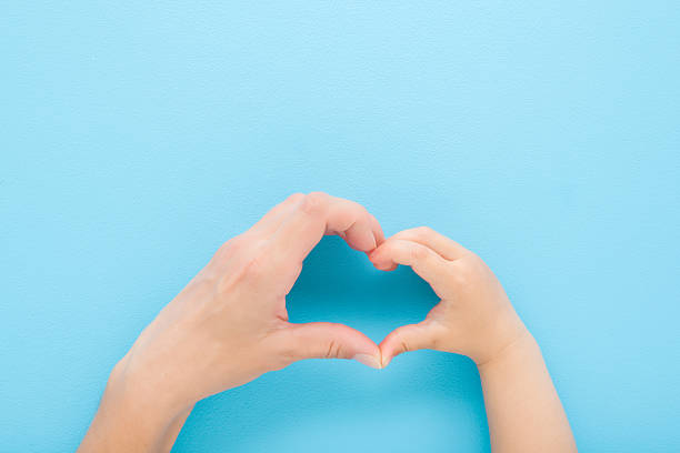 istock Heart shape created from little son and young mother hands on blue table background. Pastel color. Lovely emotional, sentimental moment. Love, happiness and safety concept. Closeup. Top down view. 2224055632